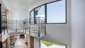 Un interior espacioso con techo alto, una escalera central y ventanas amplias que ofrecen vistas al exterior.