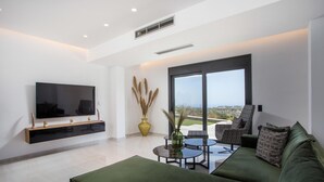 Un salón moderno con un televisor de pantalla plana, un sofá verde, una mesa de centro y un amplio ventanal con vistas.