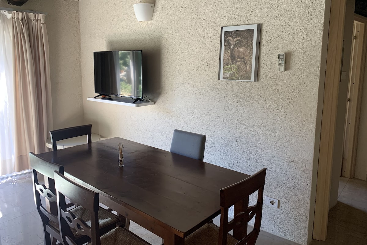 A dining area with a wooden table, chairs, a television mounted on the wall, and a framed picture.