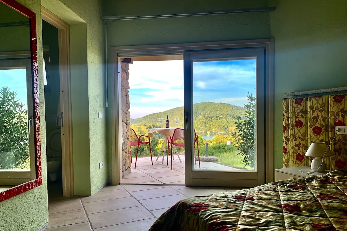 A bedroom with a bed, a window, and a view of a balcony with a table and chairs.