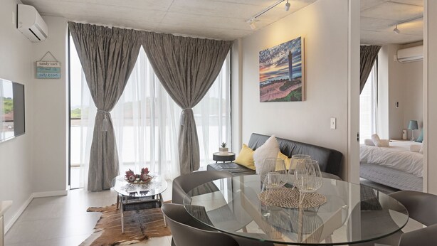 Une pièce moderne avec une table à manger en verre, un canapé gris et un tableau au mur.