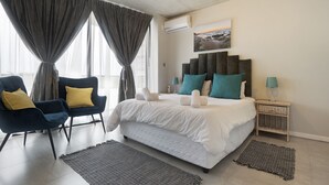 Une chambre à coucher avec un grand lit, deux fauteuils, une table de chevet et un climatiseur fixé au mur.