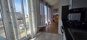 Een keuken met een magnetron, een eettafel en uitzicht op de straat door grote ramen.