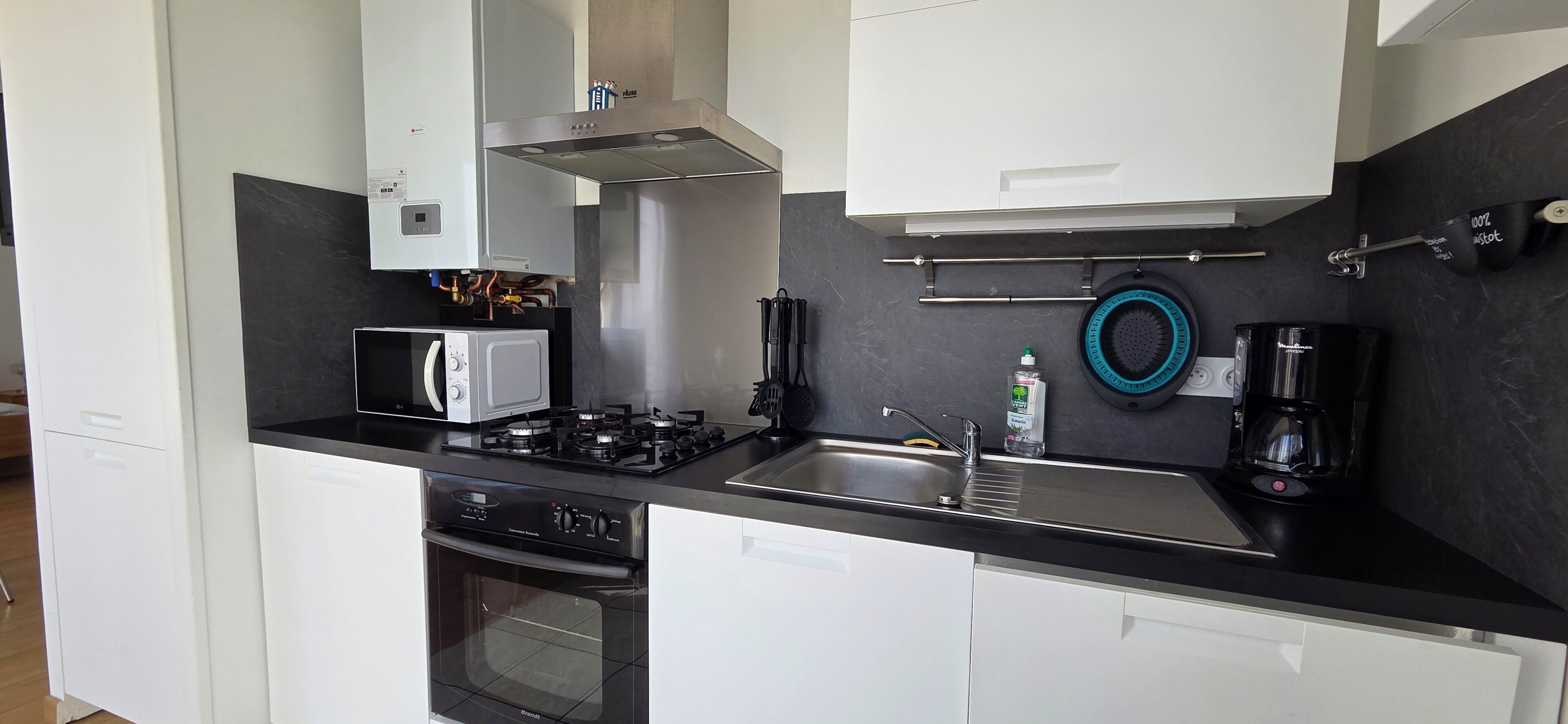 Une cuisine moderne avec des meubles blancs, un plan de travail noir, une cuisinière, un four à micro-ondes et une machine à café.