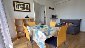 A room with a wooden dining table, chairs, a sofa, a bookshelf, and a framed picture on the wall. - Beautiful, bright apartment at Les Sables Blancs in Concarneau - 150m from the beach and the GR34 (Concarneau)
