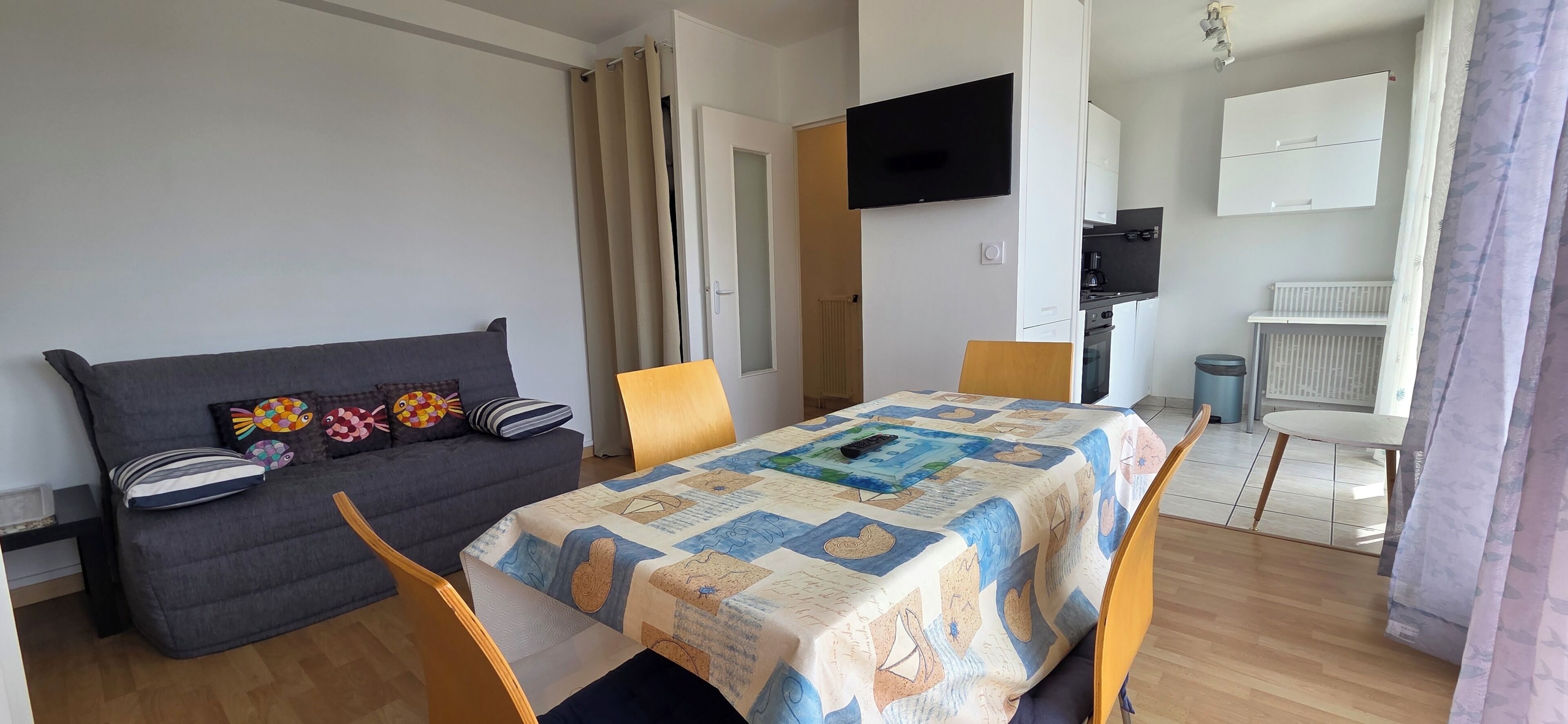 Ein gemütlicher Wohnbereich mit Sofa, Esstisch, Fernseher und Küchenzeile.