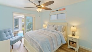 Un dormitorio con cama, ventilador de techo, mesita de noche con lámpara y una silla.