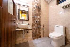 A bathroom with a wooden door, a white sink, a mirror, a toilet, and a shower area. - Itsy Hotels Adams Beach Resort, 350 Mtrs From Baga Beach (Baga)