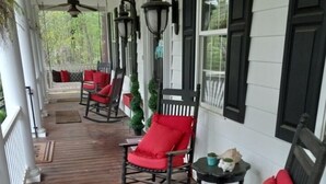 Une véranda couverte avec un plancher en bois, des fauteuils à bascule dotés de coussins rouges et une petite table sur laquelle se trouvent une tasse et une plante.