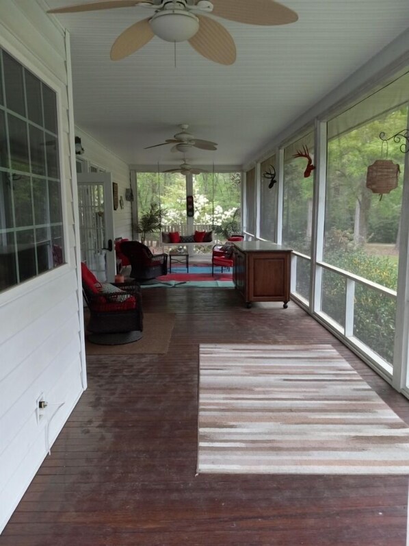 Varanda coberta com ventilador de teto, área de refeições com mesa e cadeiras e vista para o exterior.