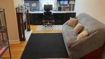 A modern living room with a grey sofa, black rug, and a kitchen area with dark cabinets and a dining table.