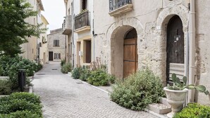 Une ruelle étroite pavée, bordée de bâtiments historiques dotés d’arcades et de balcons.