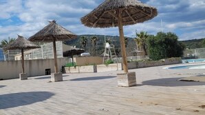 Un espace aménagé au bord de la piscine, avec des parasols en chaume, une piscine et une vue sur des collines en arrière-plan.