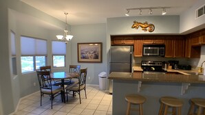A modern kitchen with a central island, wooden cabinets, stainless steel appliances, and a dining area with chairs and a table.