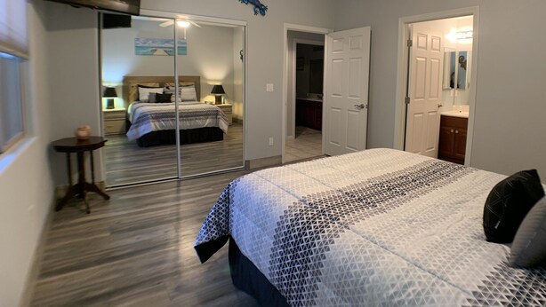 A bedroom with a bed, a ceiling fan, a TV, and a door leading to another room.