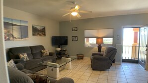A living room with a sofa, armchair, TV, and a ceiling fan.