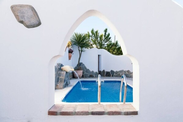 A swimming pool with a stone wall, a hanging planter, and a small waterfall feature.