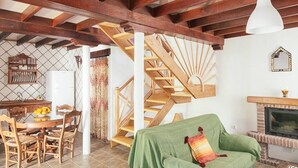A rustic interior with exposed wooden beams, a staircase, a dining area with wooden chairs, and a fireplace. - Casa Lola - House N1 in Zahora (Zahora)