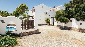 A white villa with a gravel driveway, a wooden gate, and a swimming pool visible through an archway. - Casa Lola - House N1 in Zahora (Zahora)