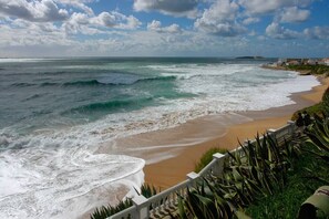 A coastal beach with waves, a sandy shore, and a staircase leading down to the beach.