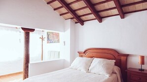 A bedroom with a wooden headboard, a bed with white bedding, a nightstand with a lamp, and a window with a view of the outside. - Casa Lola - Casa N2 en Zahora (Zahora)