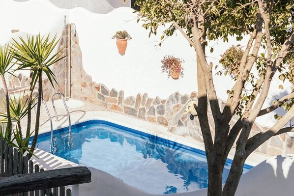 A pool area with a stone wall, potted plants, and a tree.
