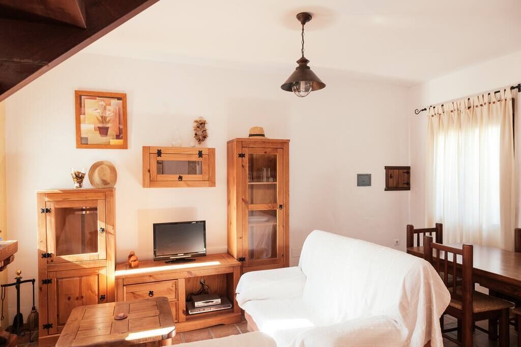 Une pièce confortable avec un bureau en bois, une télévision, un canapé blanc et une table à manger avec des chaises.
