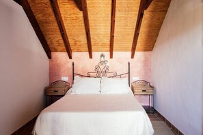 A bedroom with a wooden ceiling, a metal bed frame, white bedding, and two bedside tables with baskets.