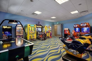 A room with arcade games, a foosball table, and a motorcycle.