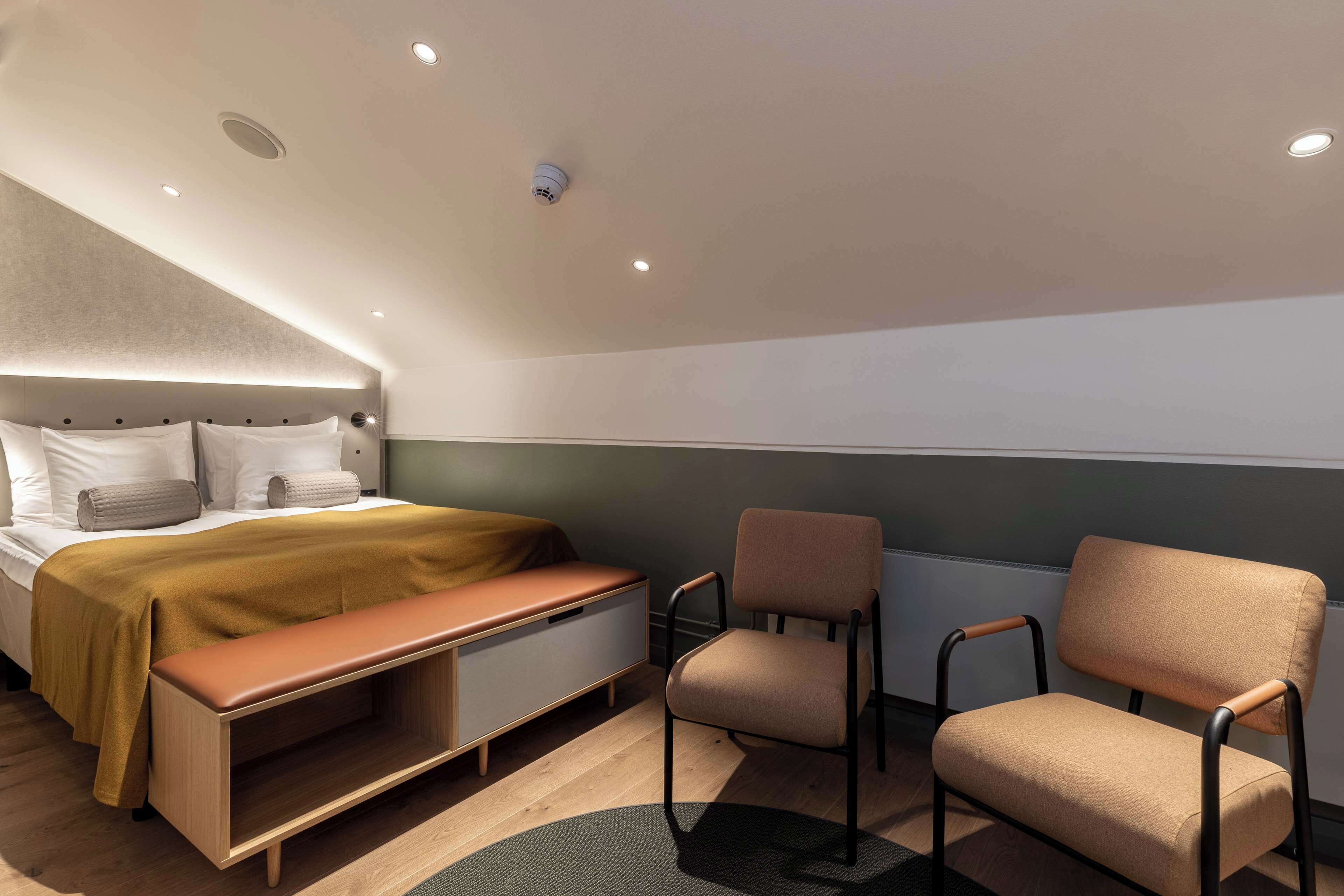 Una habitación de hotel moderna con cama, banca, sillón y escritorio.