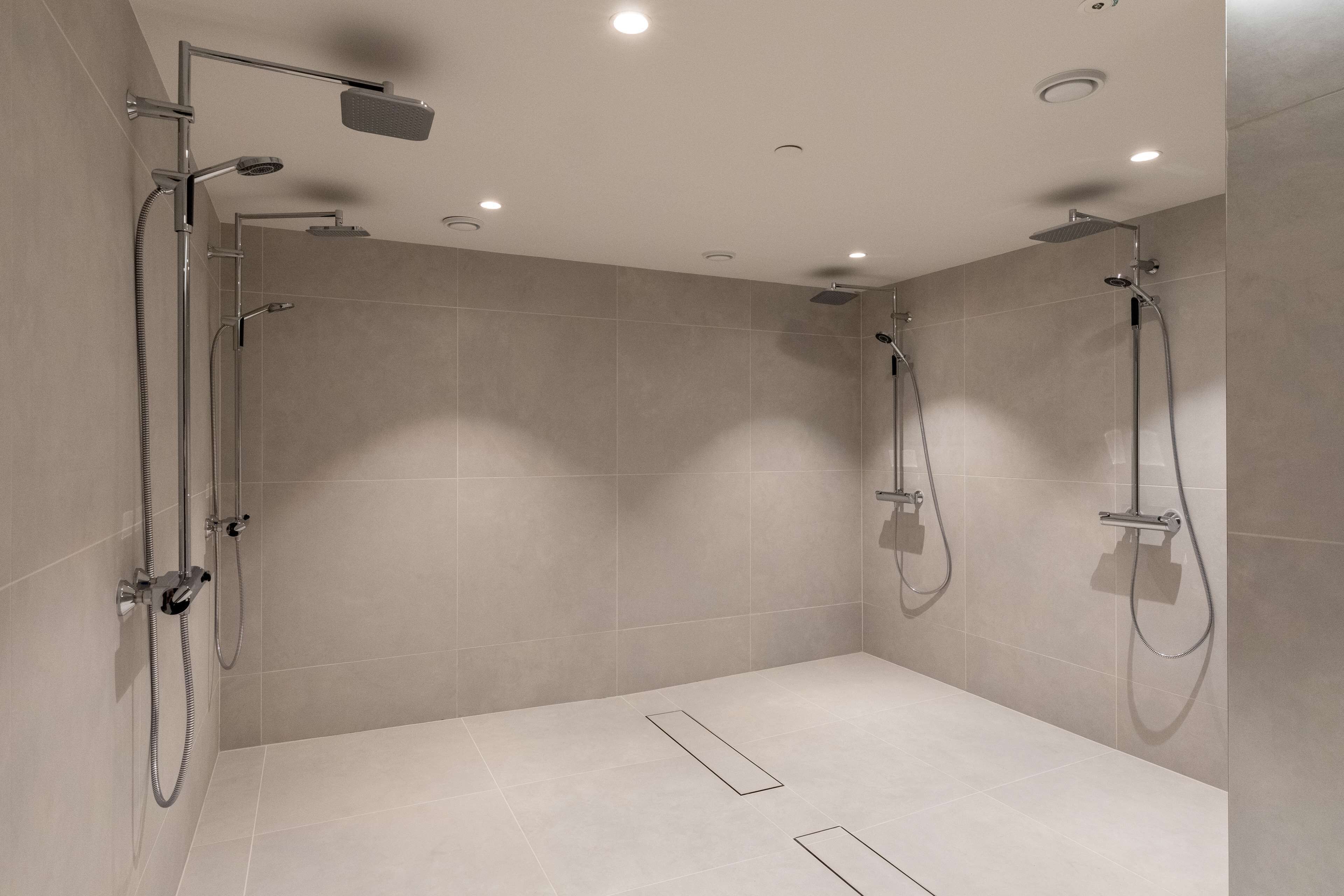 Un área de ducha moderna con dos cabezales de ducha superiores y un cabezal de ducha manual, todo instalado en una pared con luces empotradas en el techo.
