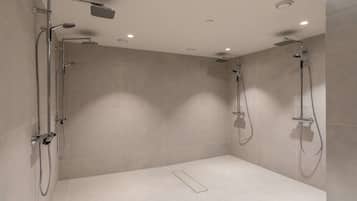 Un área de ducha moderna con dos cabezales de ducha superiores y un cabezal de ducha manual, todo instalado en una pared con luces empotradas en el techo.