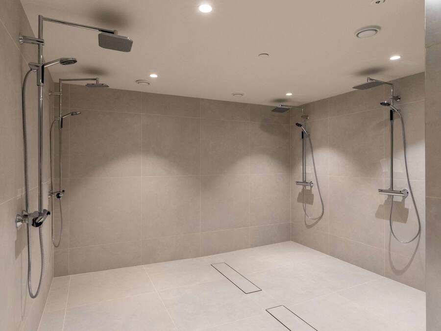 Un área de ducha moderna con dos cabezales de ducha superiores y un cabezal de ducha manual, todo instalado en una pared con luces empotradas en el techo.