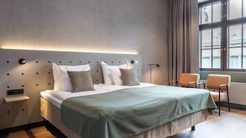 Una habitación de hotel moderna con una cama grande, una mesita de noche, una silla y una ventana con cortinas.