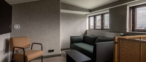 Una habitación moderna con un sofá gris, una silla marrón, una mesita y una ventana con vistas a edificios.