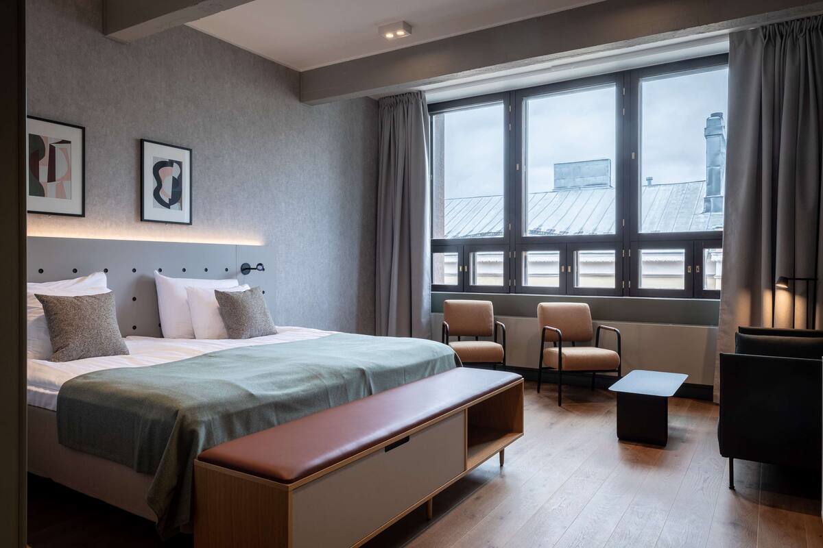 Une chambre d’hôtel moderne avec un grand lit, une banquette, deux chaises et une petite table.