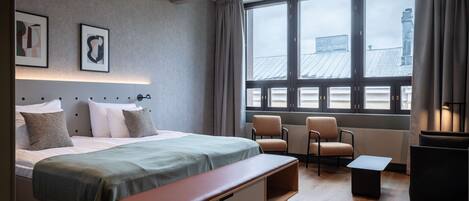 A modern hotel room with a large bed, a bench, two chairs, and a small table.