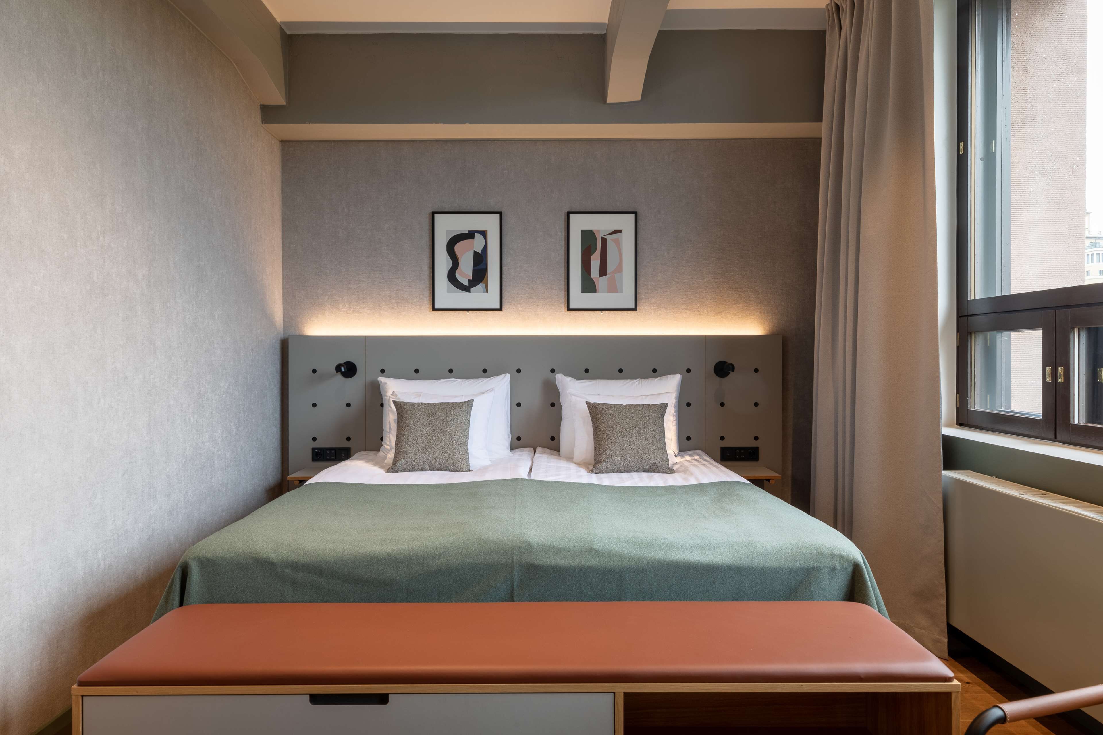 Ett hotellrum med en säng, en bänk och två inramade konstverk på väggen.