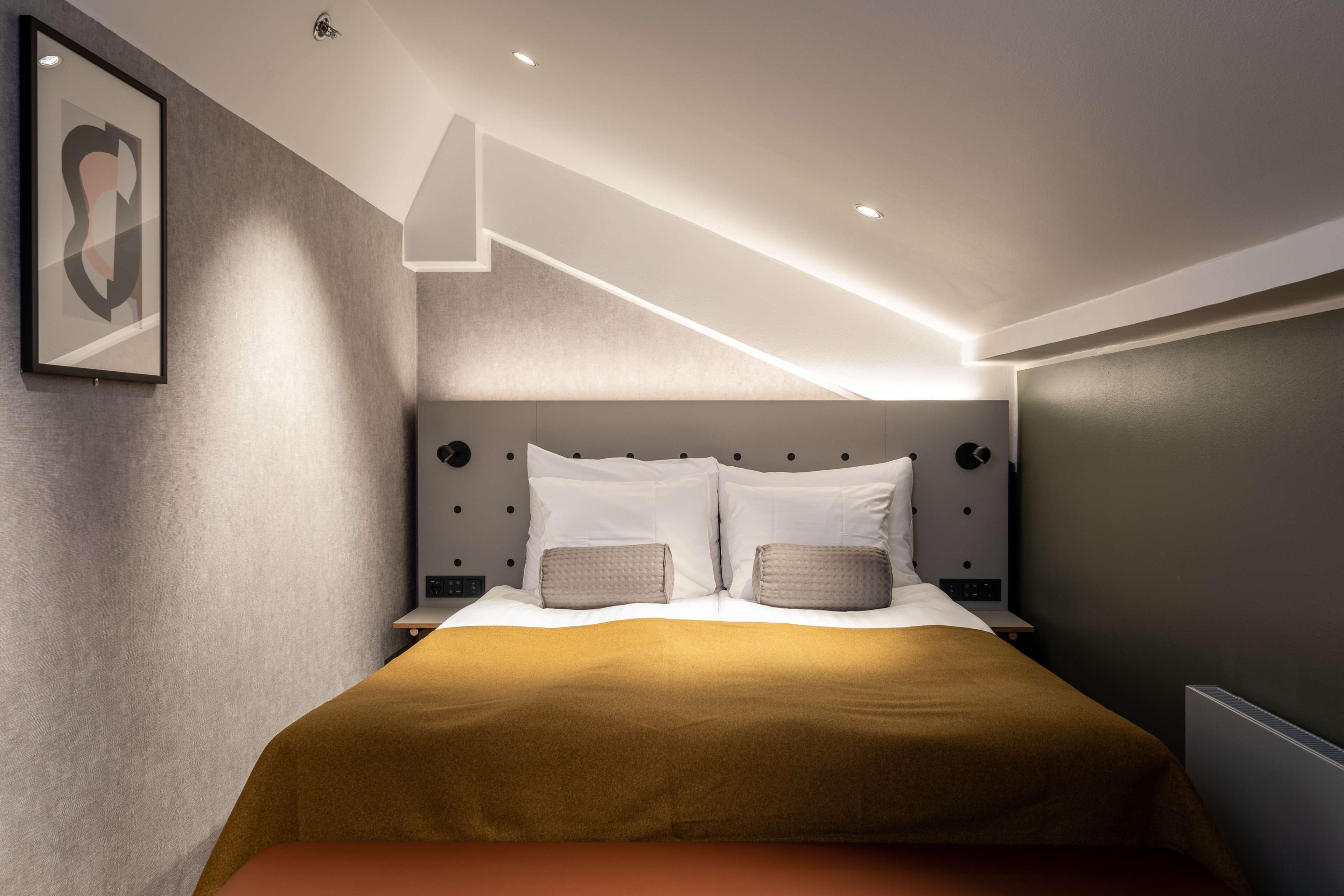 Et moderne hotelværelse med en stor seng, en sengegavl med indbygget belysning, et indramet kunstværk på væggen og et minimalistisk design.