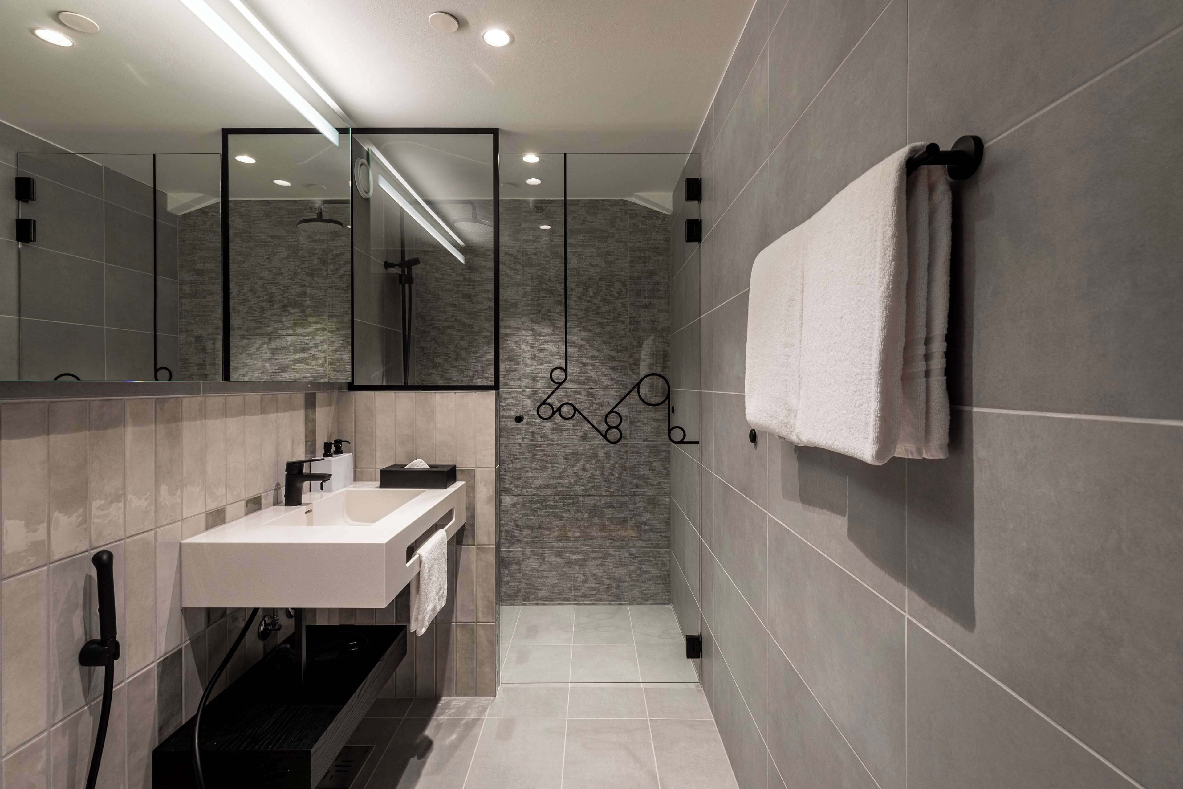 A modern bathroom with a white sink, a large mirror, and a towel rack.