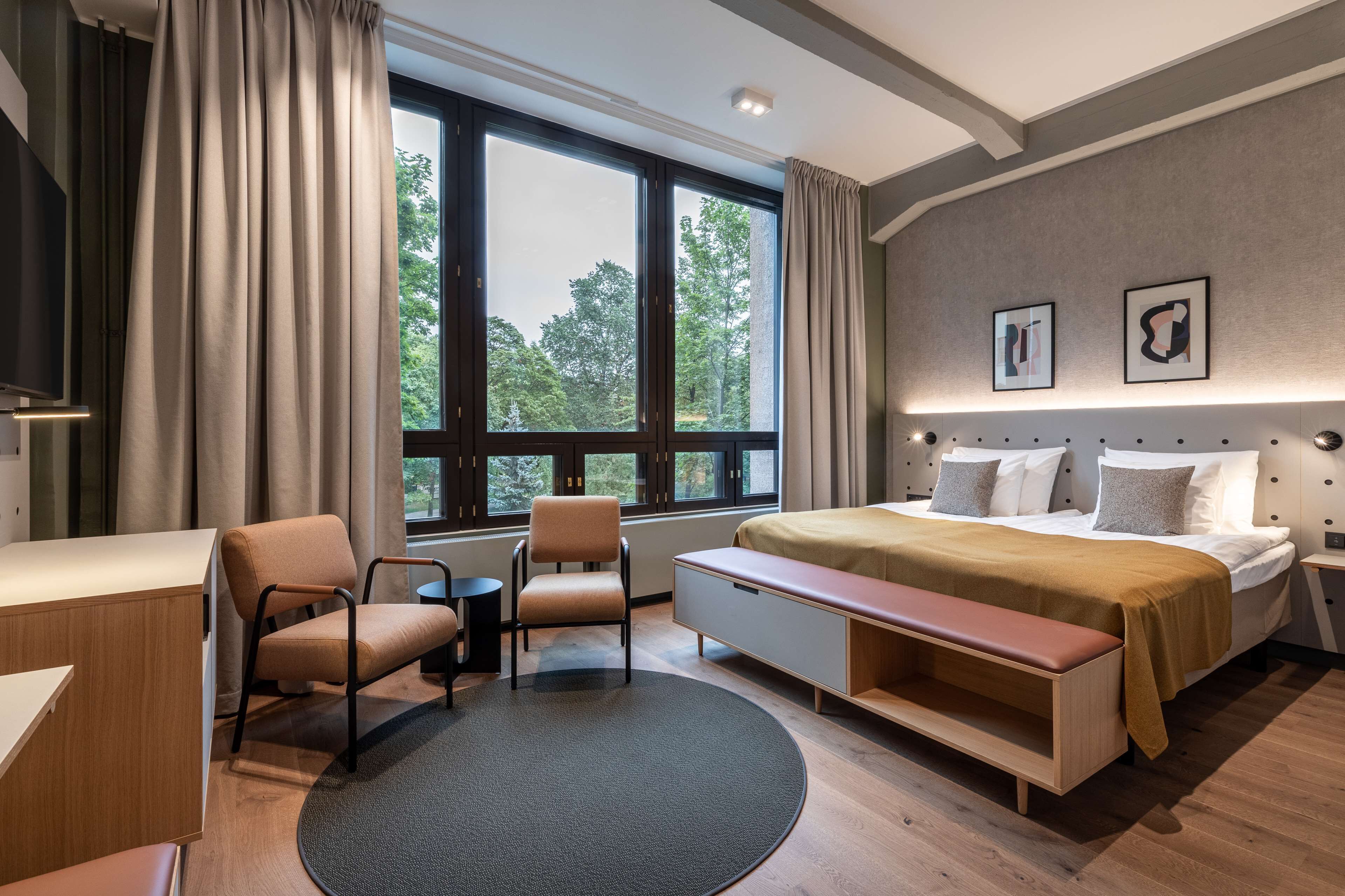 A modern hotel room with a large bed, a desk, a chair, and a bench.