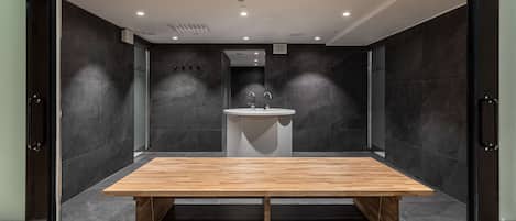 A modern bathroom with a wooden bench, a sink, and dark tiled walls.