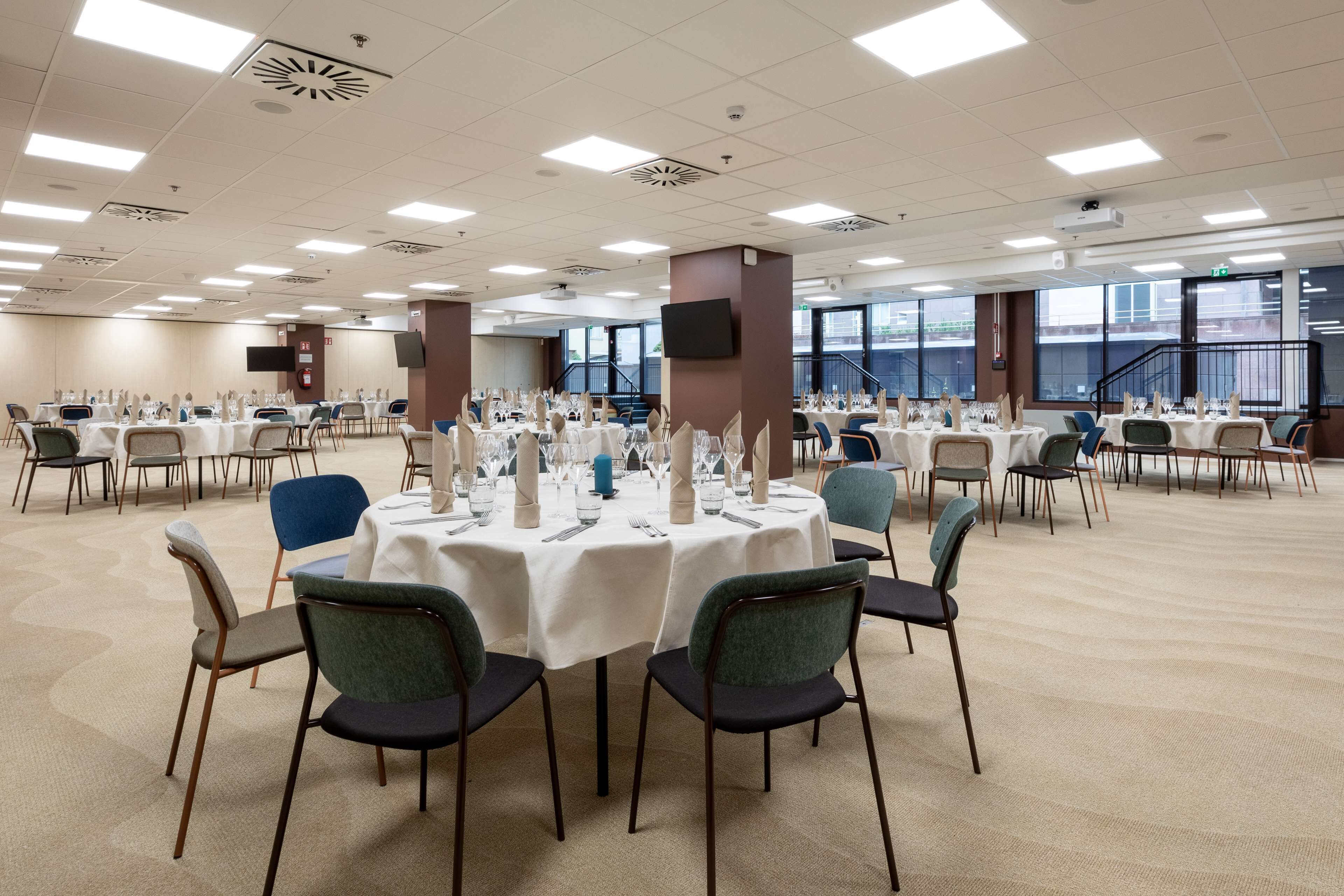 A large conference room with multiple round tables set for dining, equipped with chairs and table settings.