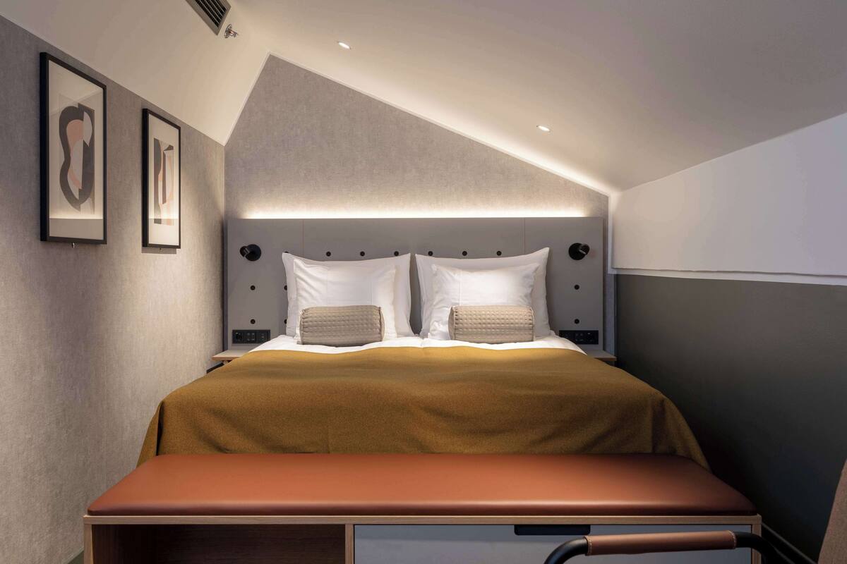 Une chambre d’hôtel moderne avec un grand lit, une table de chevet et une tête de lit dotée d’un éclairage intégré.