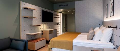 A modern hotel room with a bed, a sofa, a desk, and a TV mounted on the wall.
