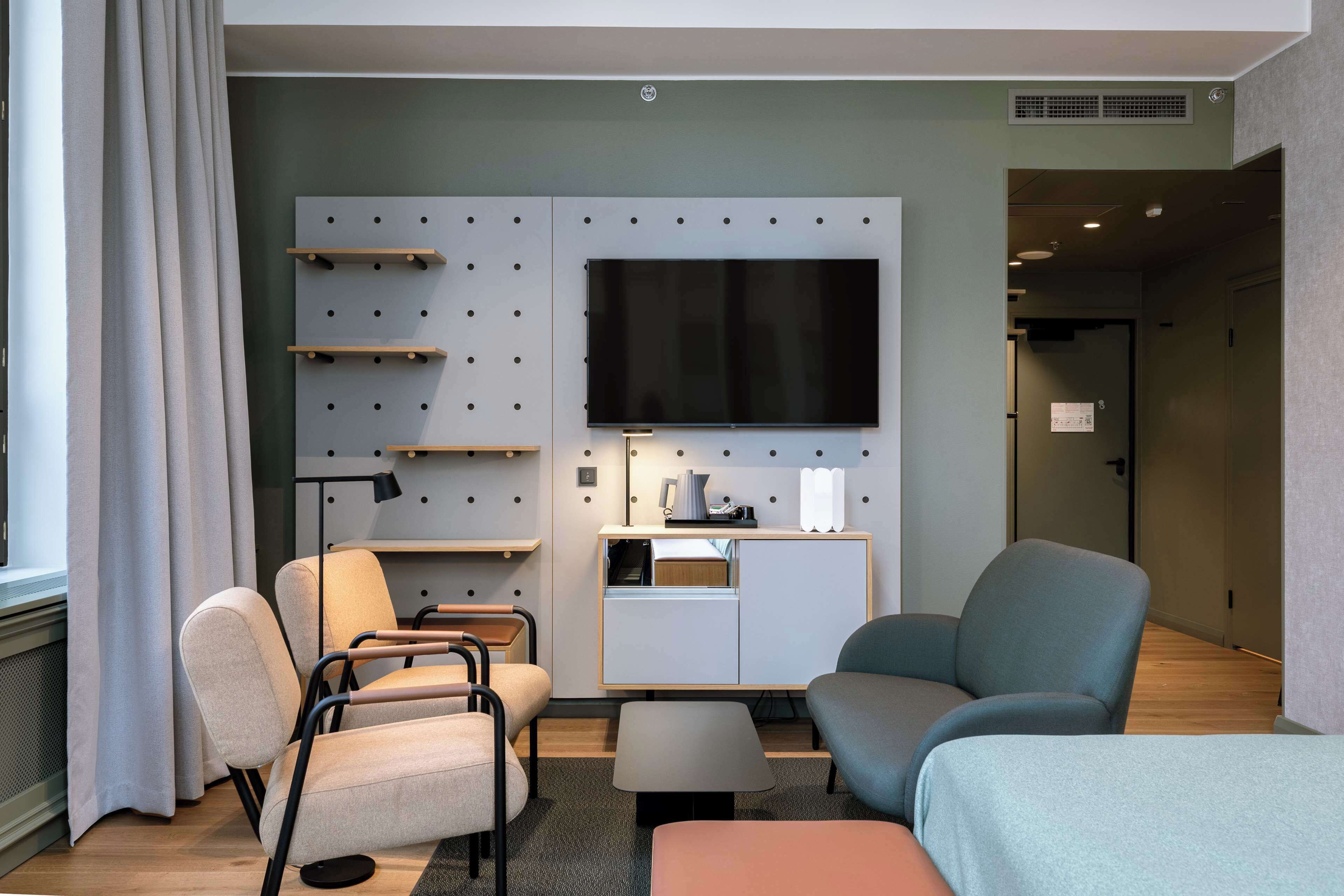 A modern hotel room with a flat-screen TV, two armchairs, a sofa, a small table, and a cabinet with a mirror.
