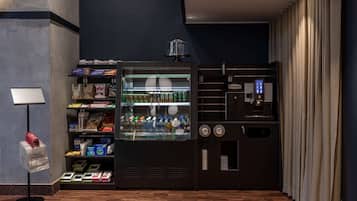 Máquina expendedora con aperitivos y bebidas, una máquina de café y una pequeña pantalla con un cartel.