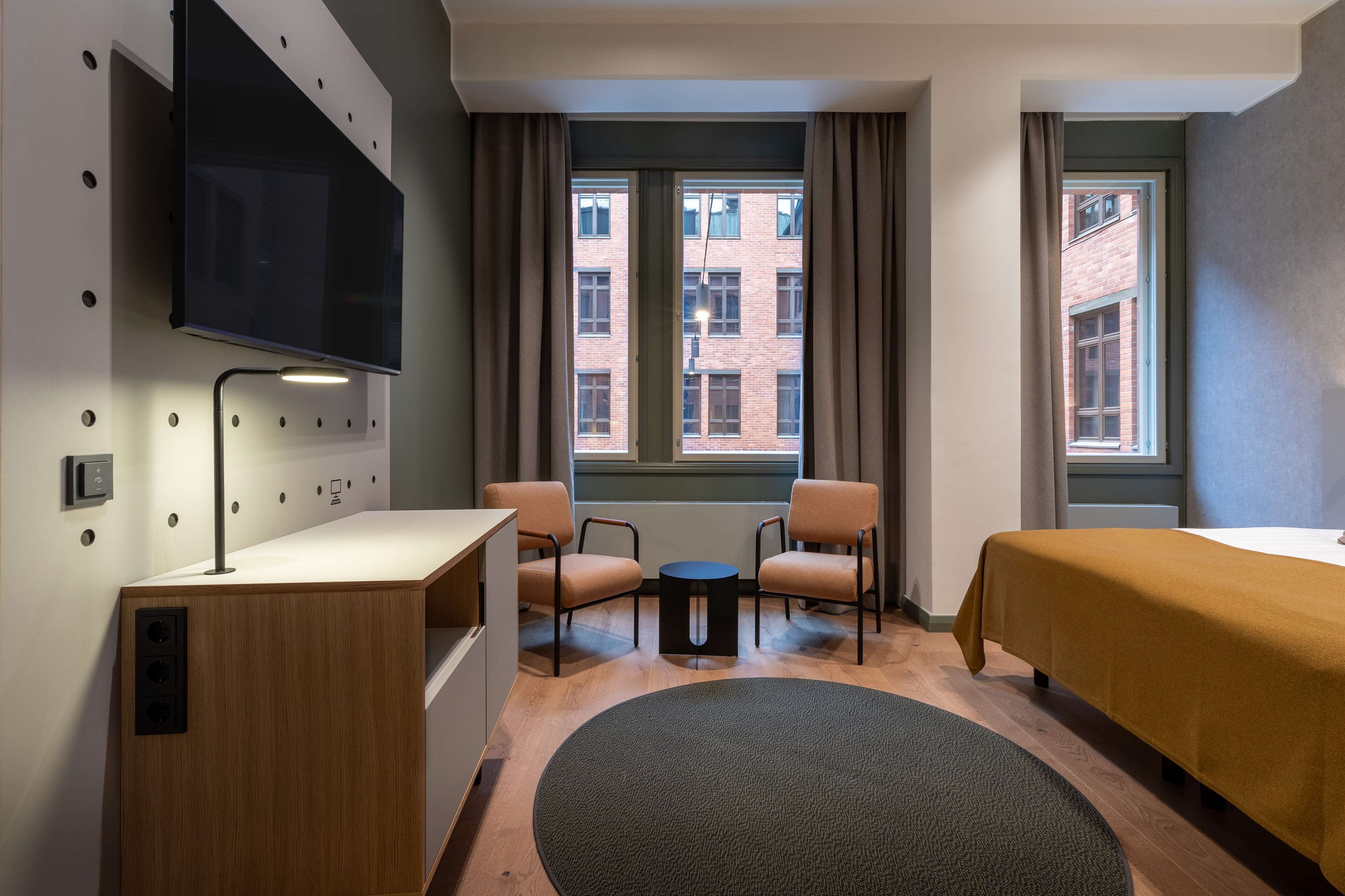 Una habitación de hotel con cama, escritorio, dos sillas, televisor y ventana con cortinas.