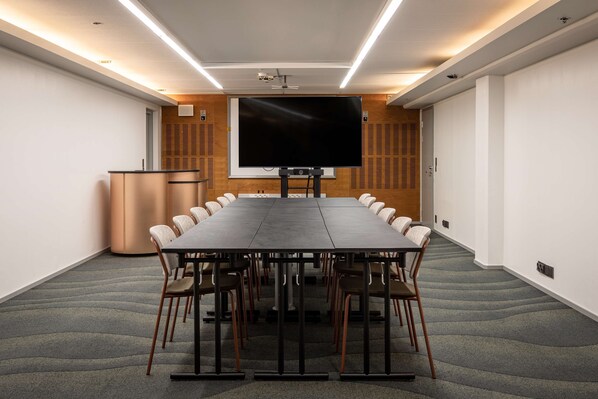 A conference room with a long table, chairs, a podium, and a large screen.