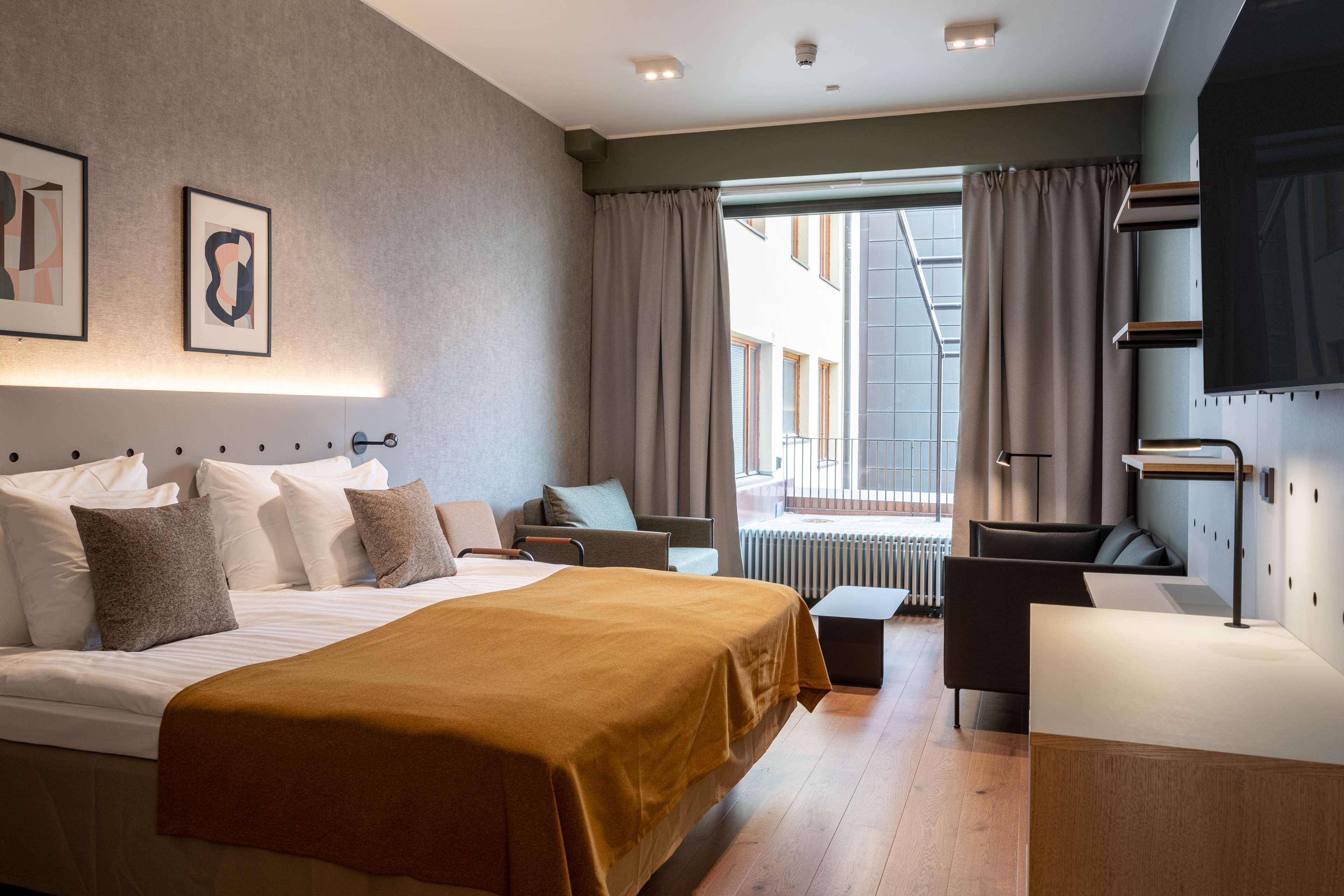 A modern hotel room with a large bed, a desk, and a view of the city.